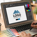 Desain logo dengan tulisan 'LOGO' di layar laptop, dengan latar belakang pensil warna dan palet warna, menggambarkan proses kreatif di ruang kerja.